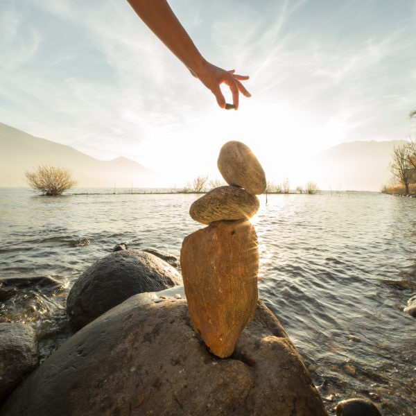 Detail of person stacking rocks by the lake. Sunset time, sunbeam.