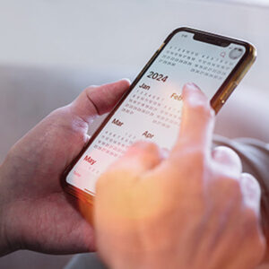 Image of a man's hands holding a mobile phone and scrolling through a 2024 calendar.