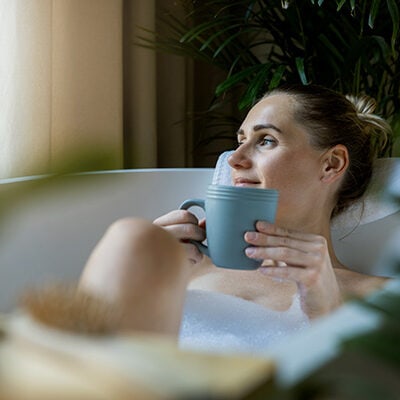 Image of a resort guest smiling gently as she enjoys a relaxing bath and a warm drink.